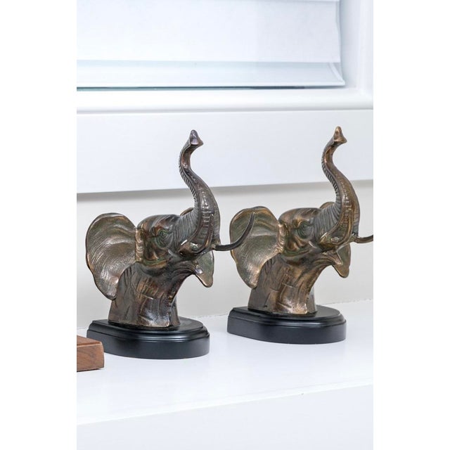 A pair of silvered finely textured bronze metalwork bookends cast as elephant heads mounted on an oval black lacquered...