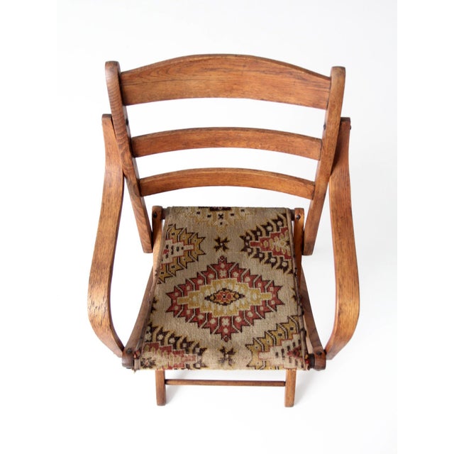 Antique folding campaign chair featuring a sculptural oak frame, softly curved arms, and a woven textile sling seat. The...