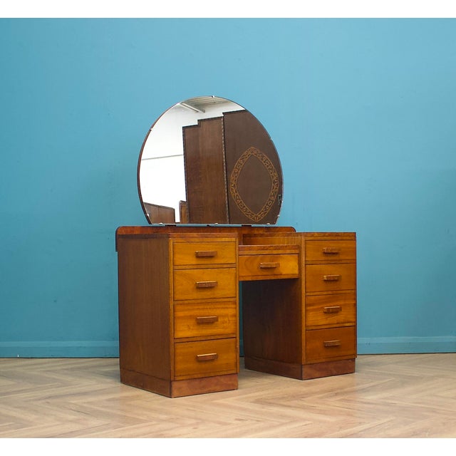 An Art Deco dressing table with a stepped top and large circular mirror set on a shaped backplate. Fitted with two banks...