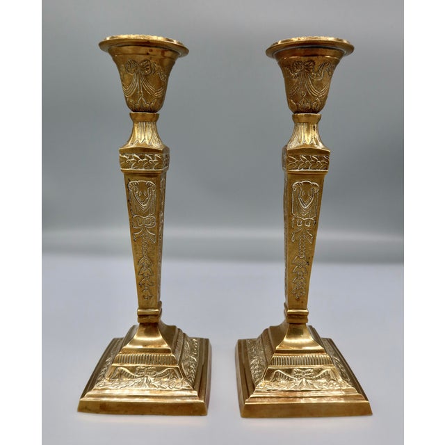 A striking pair of antique French brass-finished candlesticks in the Empire style, dating to the early 20th century. Each...