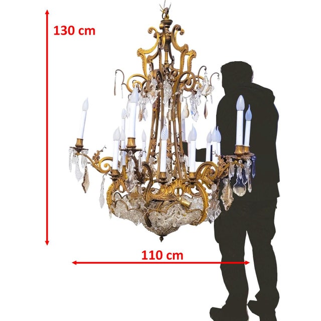 Large bronze chandelier with a gold patina, adorned with crystal drops (clear, smoky, and sometimes orange), and...