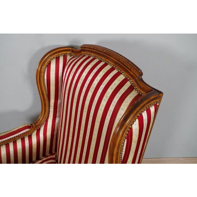 A pair of French Louis XVI style walnut bergères chairs from the 20th century with carved fluted legs and striped...