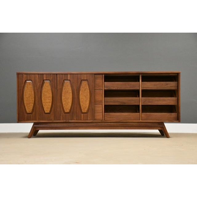A mid century modern walnut nine drawer dresser with a sliding burl accent door and canted legs made by Young...
