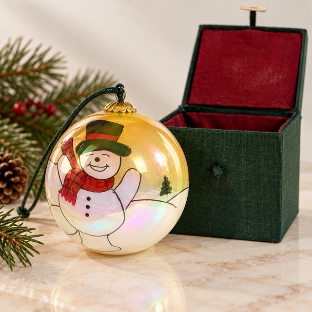 Beautiful vintage glass Christmas ornament featuring a whimsical hand-painted snowman against an iridescent golden winter...