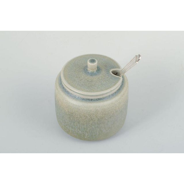 Stoneware jam jar with silver spoon. Palshus, Denmark, ca. 1960s. Cylindrical stoneware jam jar with lid. Glaze in soft...