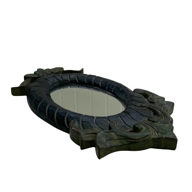 A distinctive vintage oval wall mirror surrounded by a substantial hand-carved wooden frame. The frame features deeply...