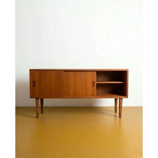 A compact 120 cm danish teak sideboard from the 1960s. Two sliding doors with carved rectangular handles flank a central...