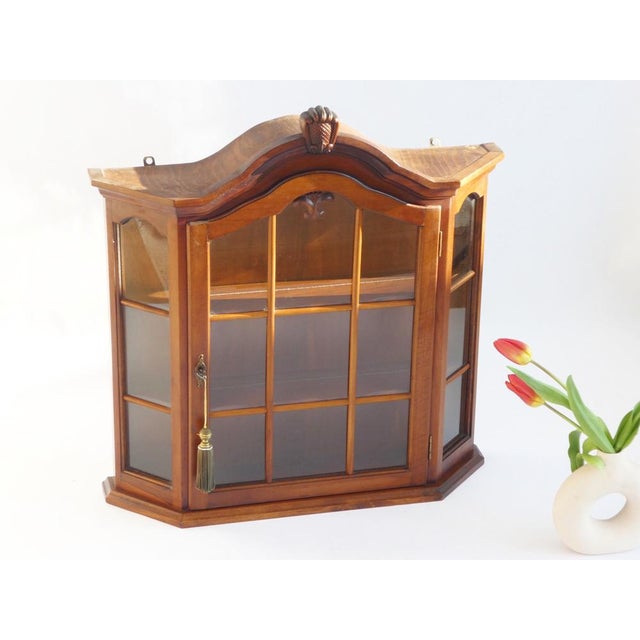 Vintage wooden wall display with glass door and shelves in the inside. It has a beautiful ornament on the top as well as...