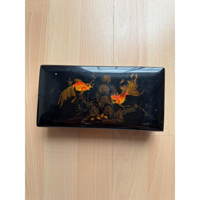 The flat, rectangular box with rounded corners is made of wood and coated all around with high-gloss black lacquer. The...