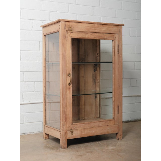 A charming vintage wooden and glass display cabinet featuring two glass sides, a glass front door, and a single interior...