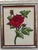 Mid-century red rose framed needlepoint features a long stemmed rose with two rosebuds and leaves on a neutral background....