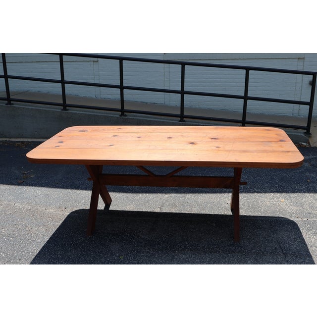 Early 20th-century American pine sawbuck dining table featuring a broad plank top, rounded corners and substantial X-form...