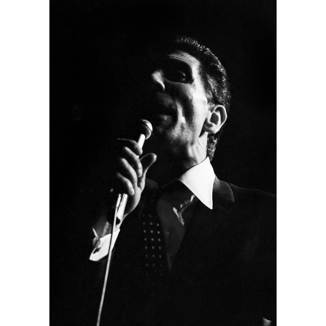 This photo shows the French singer Gilbert Bécaud during a concert in East Berlin in 1964. In the image, Bécaud is...