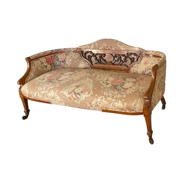 Antique Victorian low back settee featuring a carved wooden frame with floral upholstery, hand carved detail and brass...