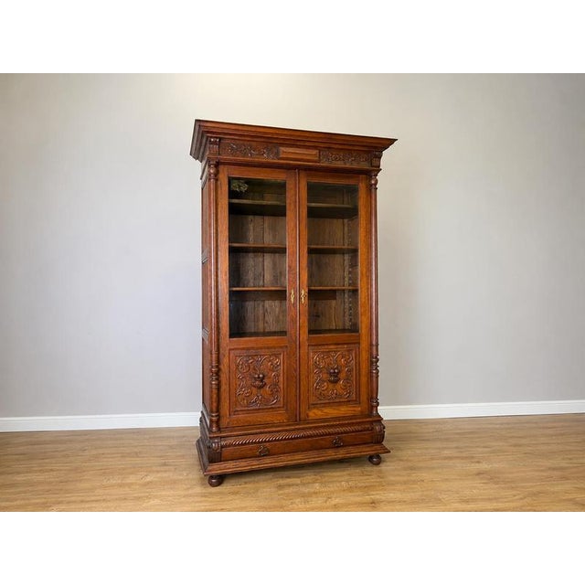 An impressive Antique French bookcase in Oak, featuring two glazed doors, elaborate carved decoration, turned column...