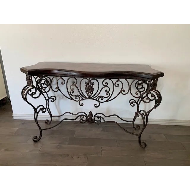 Elegant Mediterranean-style console table featuring an ornate hand-forged wrought iron base with scrolling detail and a...