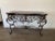 Elegant Mediterranean-style console table featuring an ornate hand-forged wrought iron base with scrolling detail and a...