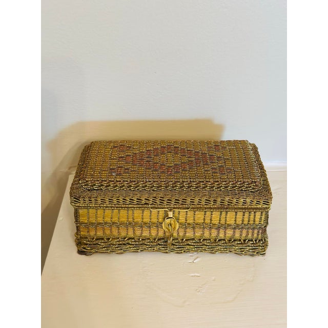 A charming vintage woven metal trinket box featuring intricate filigree-like craftsmanship in warm gold and copper tones....
