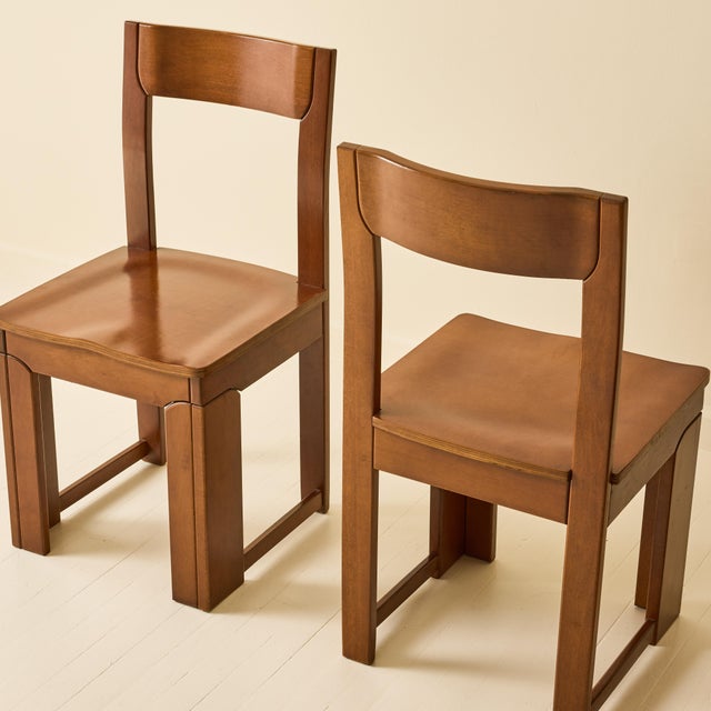 This set of six Italian dining chairs from the 1970s feature a warm walnut-toned wood with a rich, medium-brown finish....