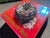 This mixed media piece presents a vibrant depiction of a colorful donut, topped with a generous sprinkle of rainbow...