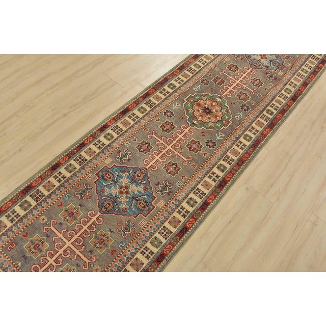A tribal Caucasian Kazak runner hand-knotted with fine wool on a cotton foundation. This rug features geometric medallions...