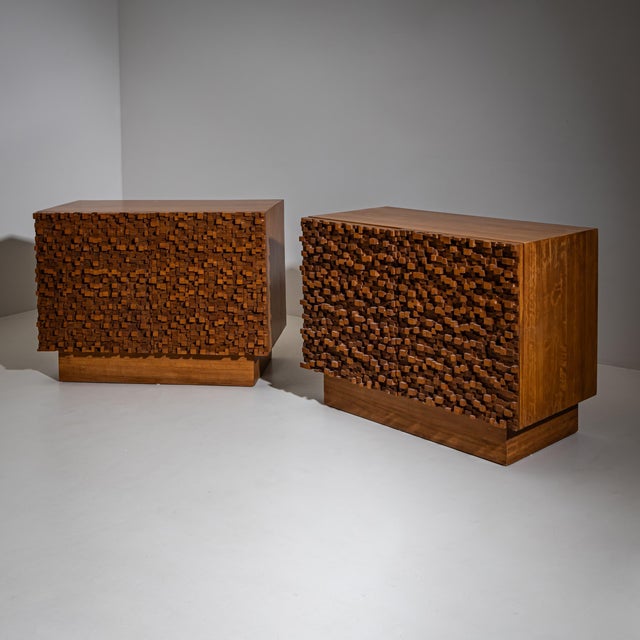 Pair of two-door wooden sideboards with clean-lined, plinth-based bodies. The doors are structured with irregular rows of...