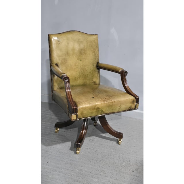 A very good mahogany swivel desk chair, pale green leather individually studded, mahogany frame, and standing on brass...
