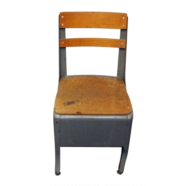 Vintage child's school chair with a steel structure and wooden seat and back. The fully enclosed lower area functions as a...