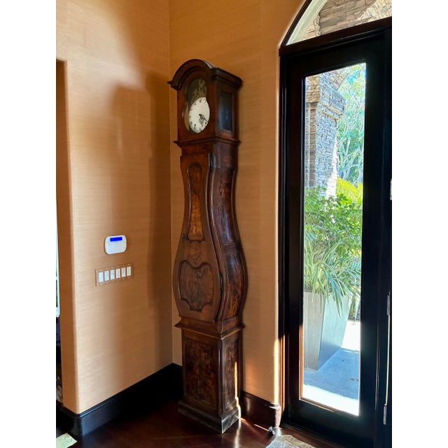 This striking antique longcase clock features an elegant French Provincial silhouette with beautifully figured burl-wood...