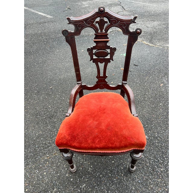 Charming carved wood side chair featuring an ornate open back and turned legs, paired with rich red upholstery that adds...