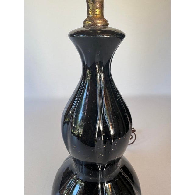 A vintage ceramic table lamp with a glossy black glaze and subtle gold spatter decoration. The elongated double-gourd form...