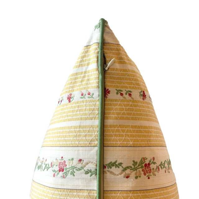 The pillow has a delicate pattern of yellow and cream stripes interwoven with floral garlands in soft green and red. The...