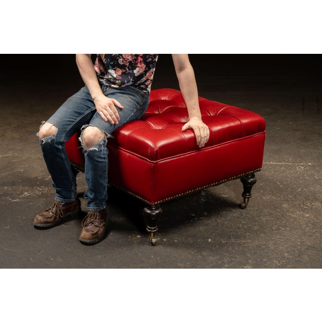Victorian-style upholstered storage ottoman. Classic tufted ottoman featuring red leather upholstery with deep button-...