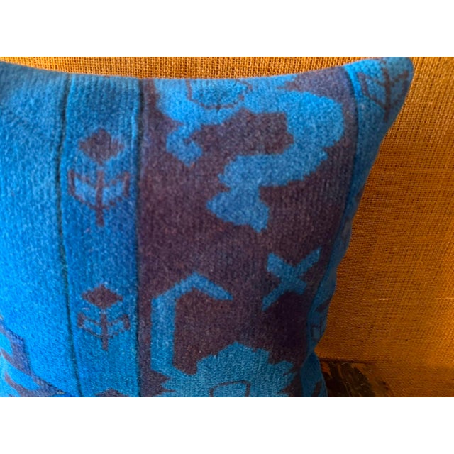Multiple woven registers move across the surface: a muted blue field patterned with angular zoomorphic forms on the left,...