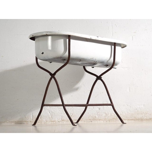 This antique bathtub in enamelled iron rests on a folding stand of bent iron tube. Originates from Central Europe, from...