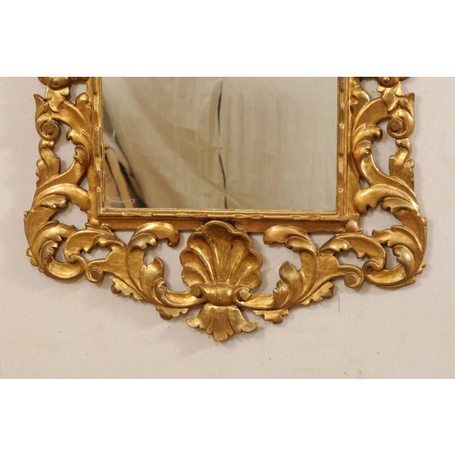 A French Rococo style carved and gilt wood mirror from the 19th century. This antique mirror from France has been designed...