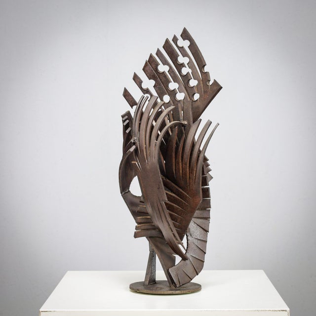 An expressive brutalist sculpture in welded iron, composed of sharply cut geometric elements that merge into a dynamic and...