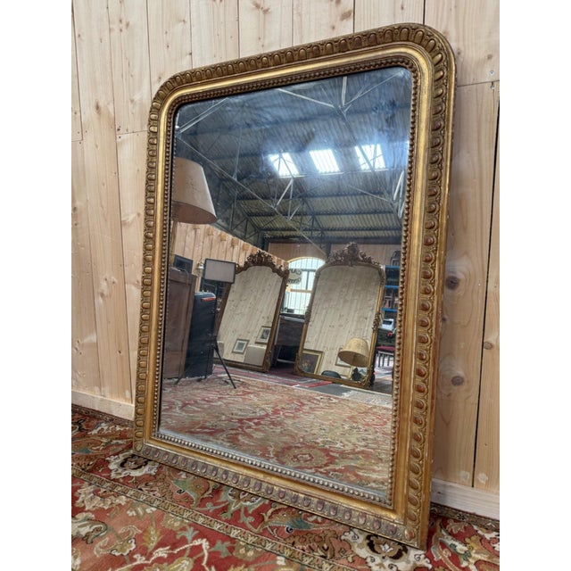 A Louis Philippe period mirror, entirely gilded with gold leaf, a remarkable testament to 19th-century craftsmanship. This...