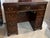 Vintage mahogany kneehole desk features decorative brass bail hardware and multiple drawers on either side. This piece is...