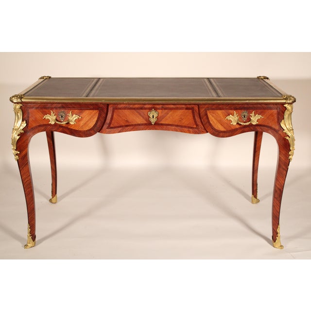 Antique Louis XV style king wood and tulip wood gilt bronze mounted desk with a tooled leather top, circa 1907. The top...
