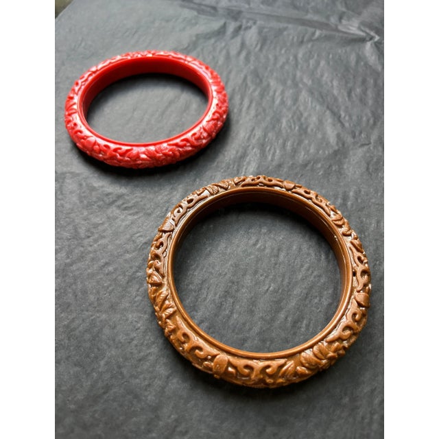This set includes two molded plastic bangle bracelets in carved floral relief—one in coral pink the other in warm brown....