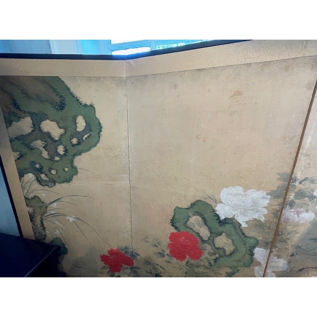A vintage Japanese folding four panel screen showcases a serene hand-painted landscape set against a warm, gilded ground....