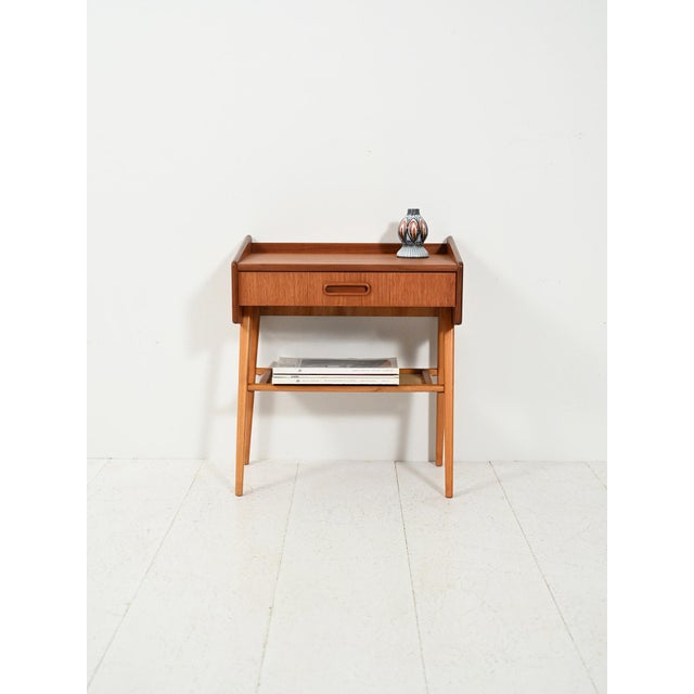 Vintage Scandinavian teak bedside table with drawer and magazine rack upholstered in raw fabric, featuring a clean,...