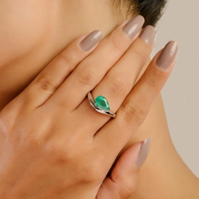 This elegant wave ring features a pear-cut Zambian emerald weighing 1.31 carats, set in 14K solid white gold. The vibrant...