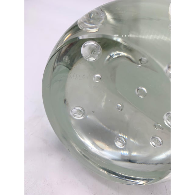 A decorative blown glass sculpture depicting a stylized bird, characterized by soft, clean lines. The body features a...