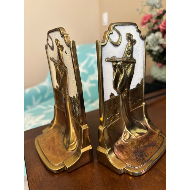 A charming pair of vintage brass and enamel figural bookends featuring a stylized female figure playing a flute, rendered...