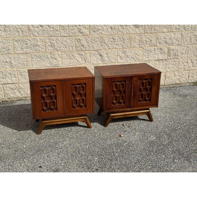 Pair of vintage Mid-Century Modern nightstands featuring sculptural geometric carved door panels, warm wood finishes, and...