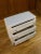 Nice vintage chest of drawers with a white patina customize with off-white wallpaper imitating crocodile skin. It opens on...