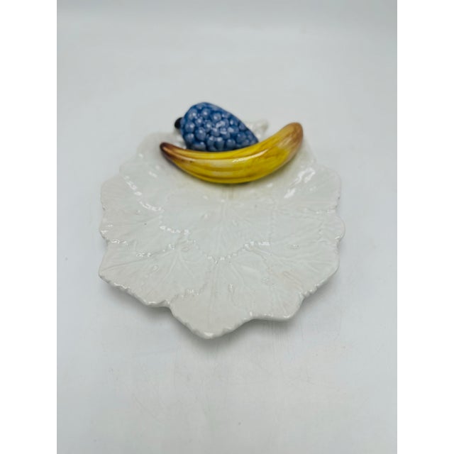 This piece is a vintage Portuguese ceramic wall plaque or dish featuring a sculpted fruit motif atop a leaf-shaped base —...