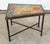 This trapezoid side table has a hand-set glass tile mosaic top in an abstract composition of red, orange, saffron, and...